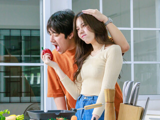 Asian young lovely lover couple husband and housewife in casual outfit standing smiling posing holding hugging cuddling while woman holding red sweet pepper in full decorated modern kitchen at home