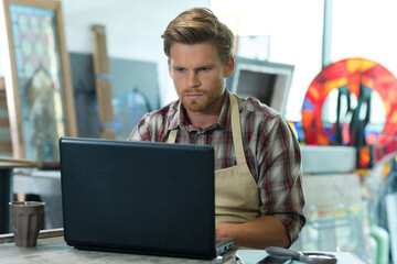 young bearded carpenter using laptop in workshop