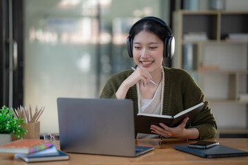 An Asian businesswoman wears headphones to meetings in video calls and takes notes data.
