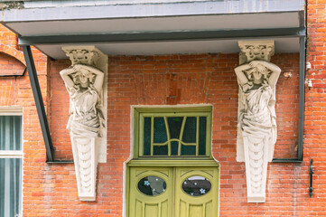A sculptural image of a standing female figure . The caryatid supports the balcony of the building....