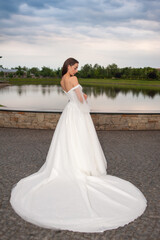 Fototapeta na wymiar Beautiful bride in wedding dress posing on sunset near lake