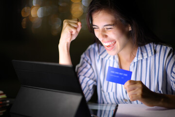 Excited woman buying online with tablet in the night