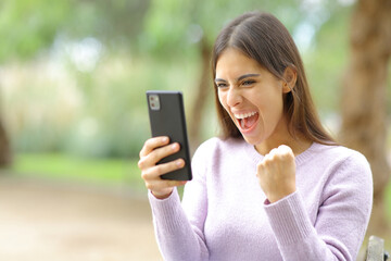 Excited woman celebrating watching phone content