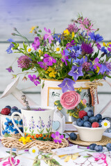 Still life with meadow flowers bouquet, berries and cup of tea in natural light, vivid wild flowers, berries in background of wooden wall, close up view