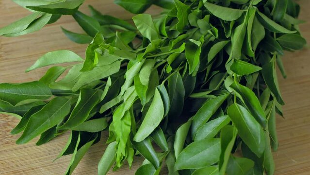 A closeup of a bunch of fresh, lush curry leaves on a wooden chop board
