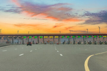 View gate for cars at the entrance to the toll road, limited by the barrier sunset evening view. Cashless payment transponder, speed limit signs.