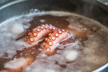 Tentacles of a raw octopus boiling in the water with salt in a big pot, close up