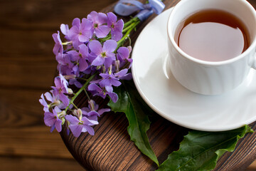 a cup of tea on a saucer. Wooden background with a bouquet of lilac flowers