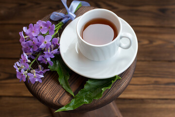 a cup of tea on a saucer. Wooden background with a bouquet of lilac flowers