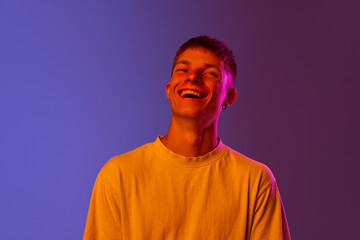 Portrait of young guy cheerfully laughing against gradient purple background in neon light. Happiness and joy. Concept of human emotions, youth, lifestyle, fashion, facial expressions, ad