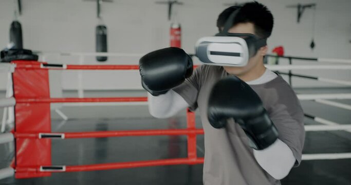Young man wearing boxing gloves training in gym using virtual reality glasses enjoying leisure time. Modern technology and sports concept.