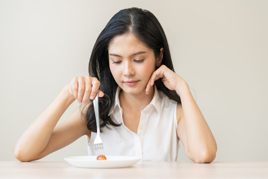 Diet in bored face, unhappy beautiful asian young woman, girl on dieting, holding fork at tomato on plate, dislike or tired with eat fresh vegetables. Nutrition of clean, healthy food good taste.