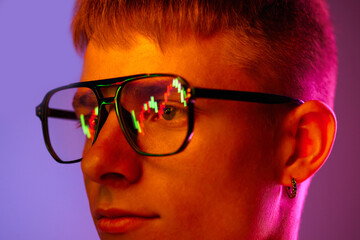 Close-up of young man in glasses with trading graphs reflection. Model against gradient purple background in neon light. Concept of human emotions, youth, lifestyle, fashion, facial expressions, ad