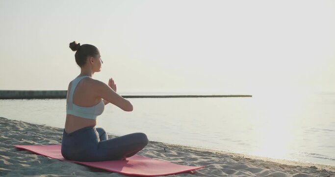 Young woman meditating on beach in morning. Camera moving around girl