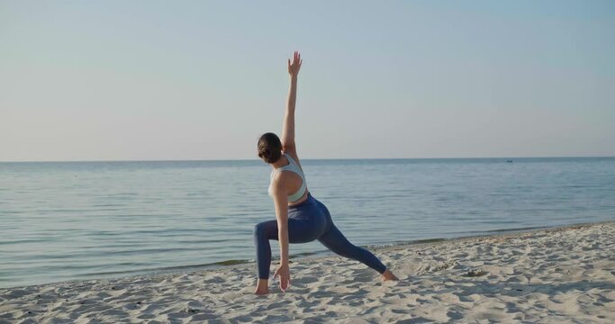 Sporty young woman practicing yoga on beach near sea in morning