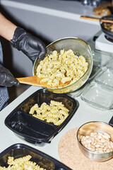Vertical closeup of female hands putting pasta into plastic containers while working in food delivery or doing meal prep, copy space