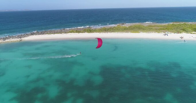 Red kite surfer sails through crasky los roques island catching air above blue ocean water