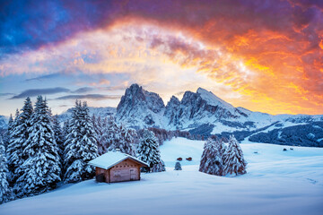 Picturesque landscape with small wooden log cabin on meadow Alpe di Siusi on sunset time. Seiser Alm, Dolomites, Italy. Snowy hills with orange larch and Sassolungo and Langkofel mountains group - Powered by Adobe