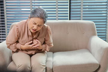 Asian senior woman sitting and suffering from chest pain or heart attack from working accident on...