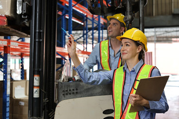 Group of warehouse workers with hardhats and reflective jackets using tablet, walkie talkie radio and cardboard while controlling stock and inventory in retail warehouse logistics, distribution center