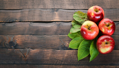 Fresh red apples with green leaves on wooden table. On wooden background. Free space for text . Top...