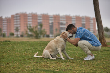 Young Hispanic man, crouching on the grass joining his forehead with his dog's forehead in loving and tender attitude. Concept, dogs, pets, animals, friends.