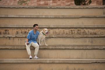 Young Hispanic man, sitting on large cement stairs next to his dog looking both in the same direction. Concept, dogs, pets, animals, friends.