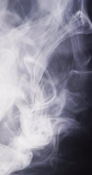 Vertical video of white clouds of smoke moving with copy space on black background