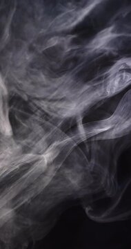 Vertical video of white clouds of smoke moving with copy space on black background