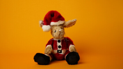 Plush bunny in Santa Claus costume on a yellow background.