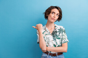 Photo of doubtful unsure lady wear print shirt showing thumb looking empty space isolated blue...