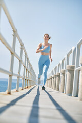 Smiling sportswoman running on bridge during cardio training