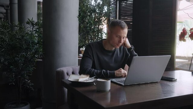 Handsome Caucasian Man With Laptop Surfing Internet Sitting In Cafe In Daytime, Using Free Wi-Fi