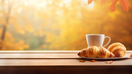 A cup of coffee and croissant on a wooden table with an autumn blurred background with a place for...