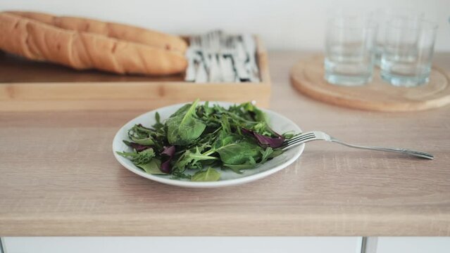 Delicious healthy meal with fork in kitchen. White bowl with fresh salad stands on table closeup