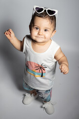 Bebé sonriente con gafas de sol de corazones vestido con estampado palmeras. Concepto moda de bebé.