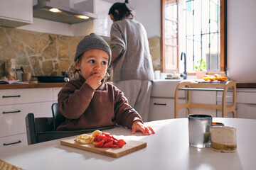 Cute little boy eating fruits in kitchen