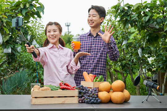 한국 전원생활 농촌 쇼호스트 농장에서 농작물 셀카봉 들고 라이브커머스 방송 진행하는 젊은청년 부부 커플 모습