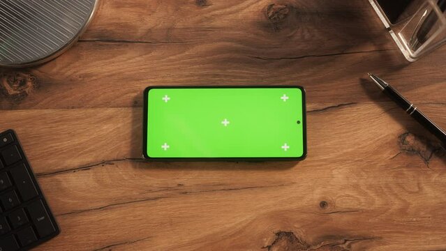 Top Down View of a Smartphone with Mock Up Green Screen Chromakey Display with Motion Tracker Placeholders. Static Footage of a Cellphone Device Lying Horizontally on a Wooden Office Table