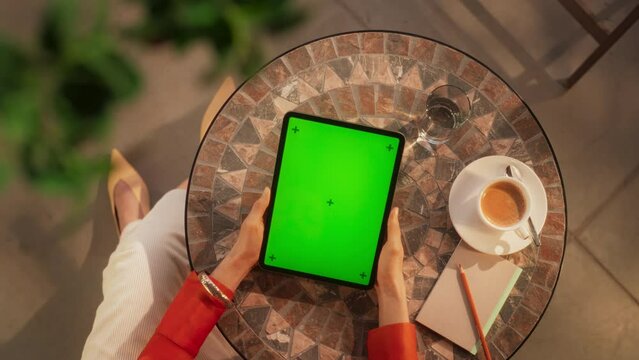 Top View of Anonymous Female Using a Digital Tablet Computer with Mock Up Green Screen Chromakey Display in a Cafe. Elegant Woman Reading her Favorite E-book While Relaxing and Drinking Coffee