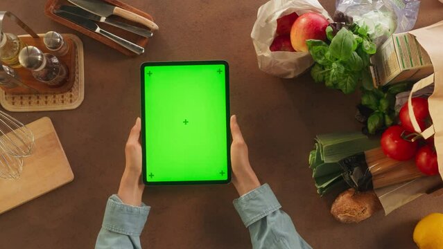 Top View of Anonymous Female Using a Digital Tablet Computer with Mock Up Green Screen Chromakey Display on a Kitchen Table. Woman Getting Inspired by her Favorite Recipe E-book While Preparing Dinner