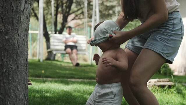 Young mother puts a T-shirt on her young son in the garden on a sunny day