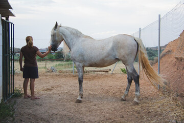 Mujer de espaldas acariciando el hocico de su caballo