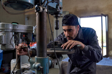 Focused ethnic mechanic working with vertical drill in garage