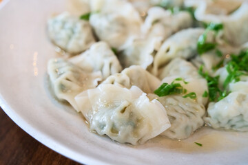 Fresh, delicious boiled garlic chives dumplings, jiaozi in white plate on wooden table background.