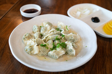 Fresh, delicious boiled garlic chives dumplings, jiaozi in white plate on wooden table background.
