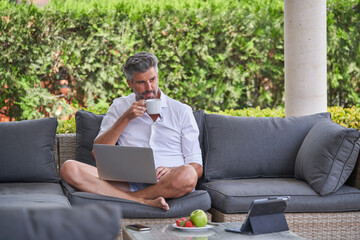 Businessman with laptop drinking coffee in backyard