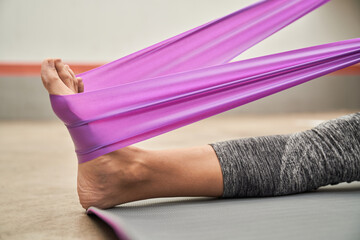 Anonymous sportswoman stretching leg with resistance band