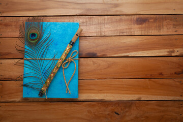 Beautiful Blue colored textured Diary made with handmade paper, Peacock feathers, and a flute on the top. Wooden background. Top view.