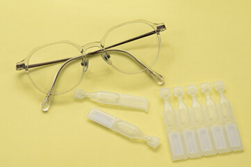 노랑배경 위의 안경과 일회용 안약